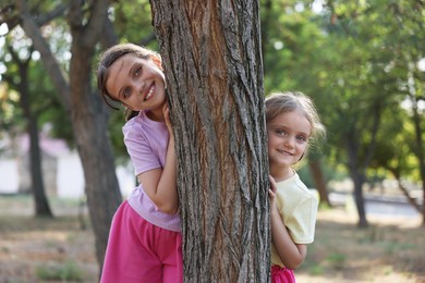 Photo of Cute little sisters hiding behind tree in park