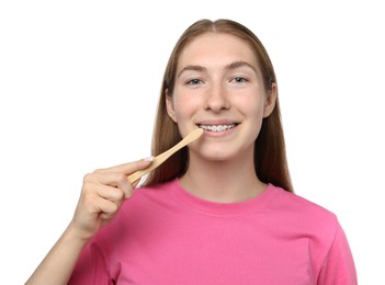 Photo of Smiling girl with braces cleaning teeth on white background