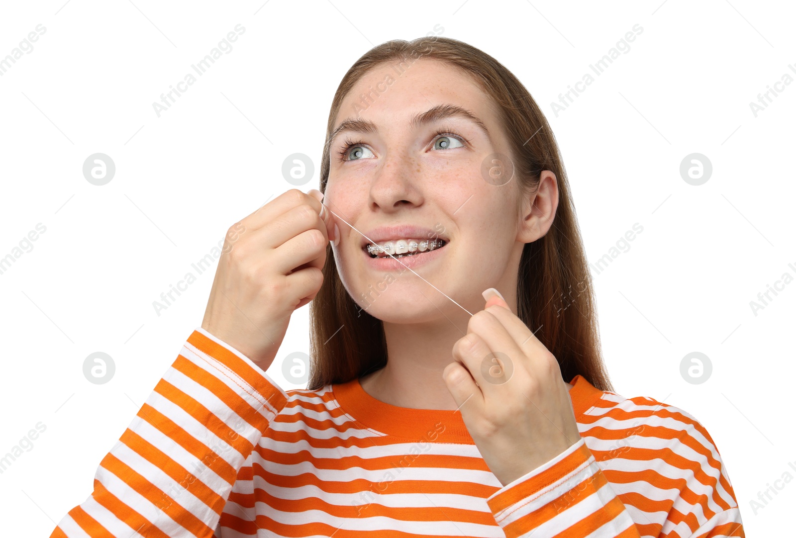 Photo of Smiling girl with braces cleaning teeth with dental floss on white background