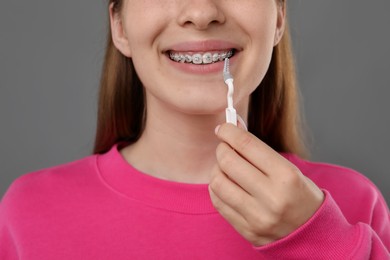 Photo of Girl with braces cleaning teeth with interdental brush on grey background, closeup