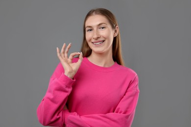 Photo of Smiling girl with braces showing ok gesture on grey background