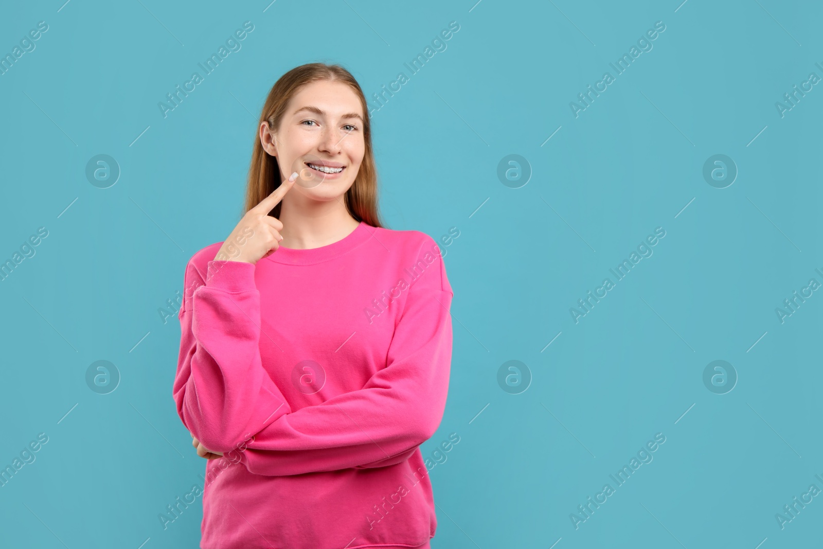 Photo of Girl pointing at her braces on light blue background, space for text