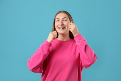 Photo of Girl with braces cleaning teeth with dental floss on light blue background