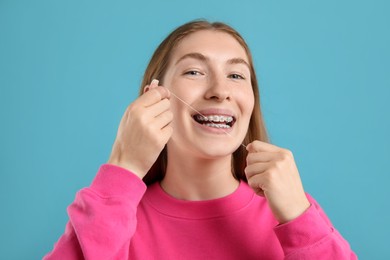 Photo of Girl with braces cleaning teeth with dental floss on light blue background