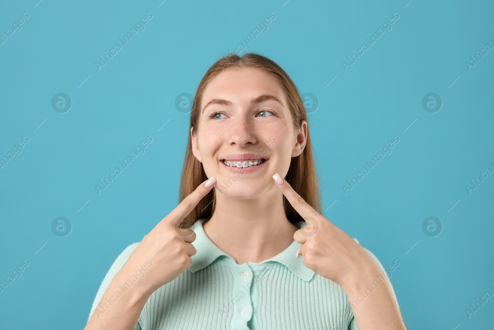 Photo of Girl pointing at her braces on light blue background