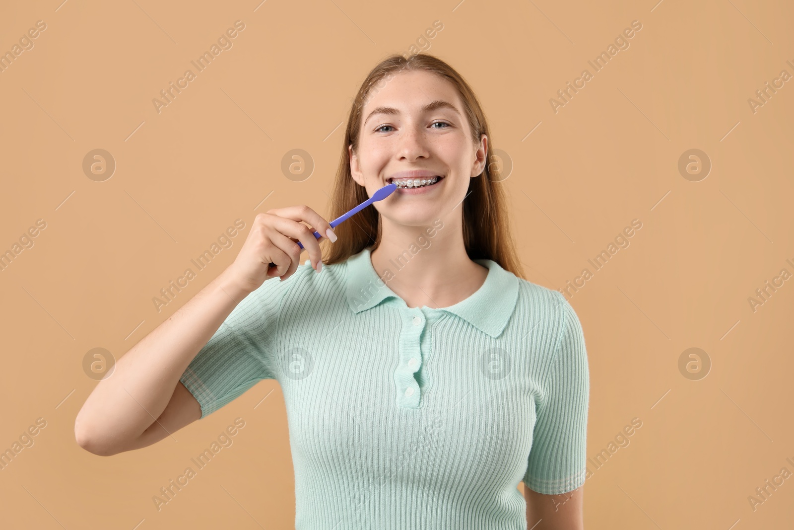 Photo of Girl with braces cleaning teeth on beige background