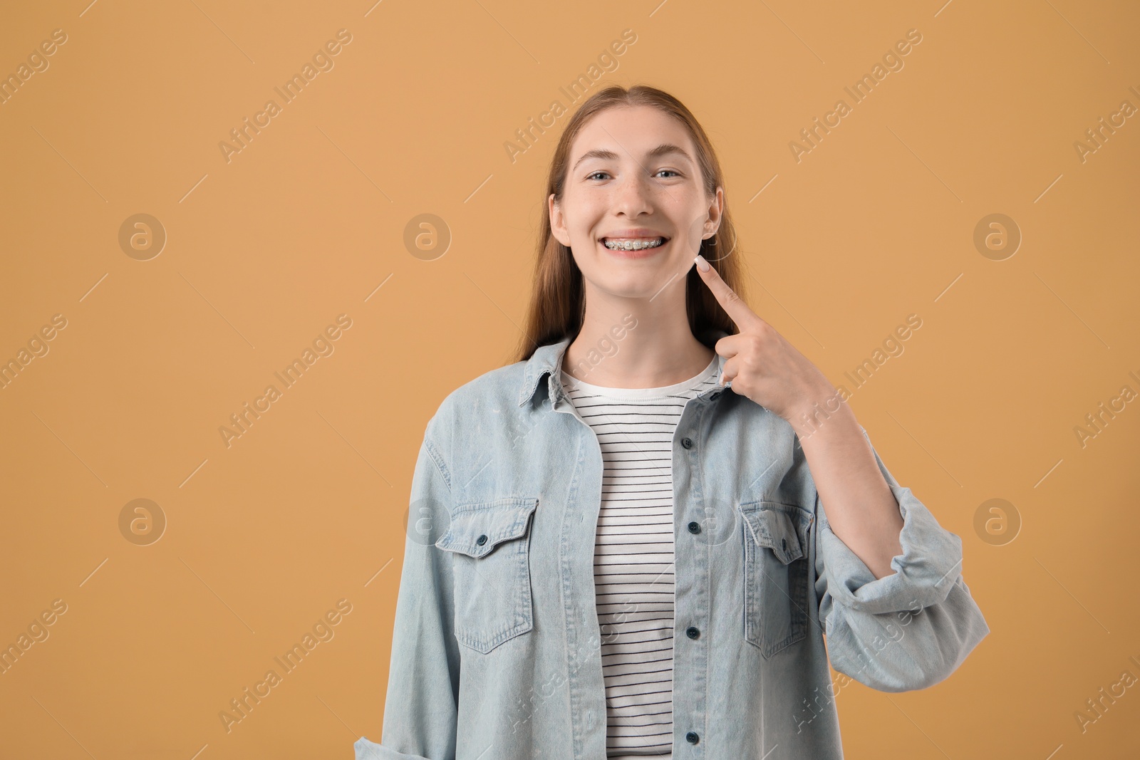 Photo of Girl pointing at her braces on beige background, space for text