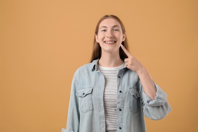 Photo of Girl pointing at her braces on beige background, space for text