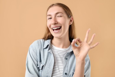 Photo of Smiling girl with braces showing ok gesture on beige background