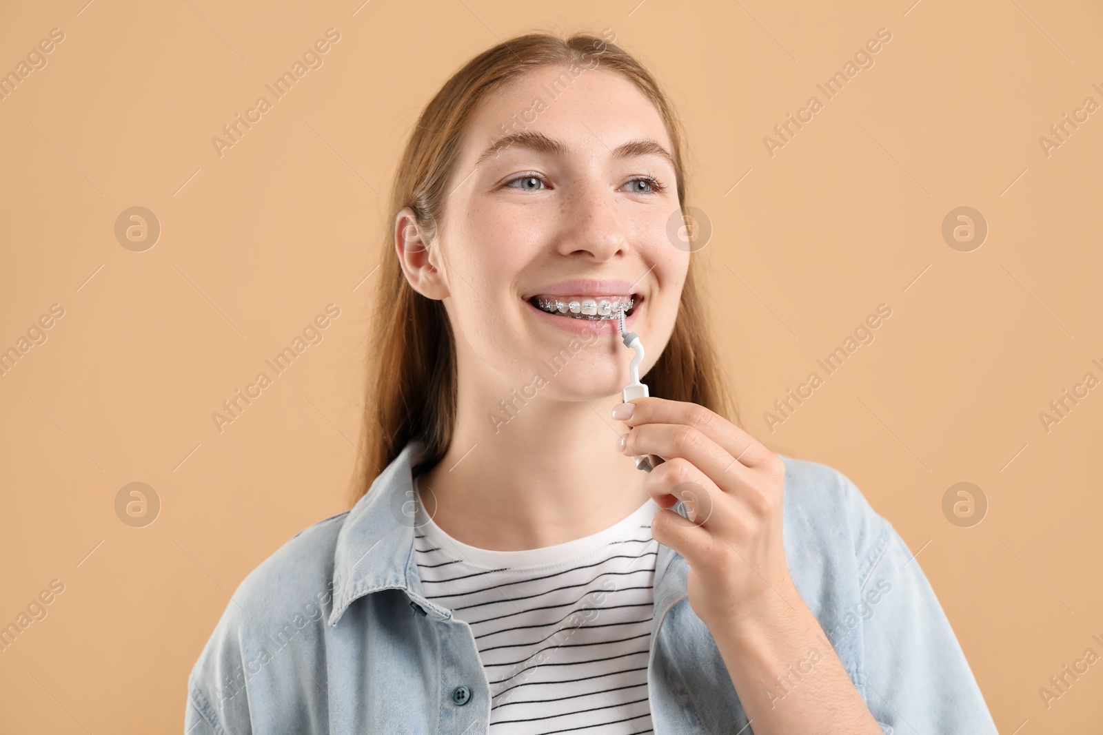 Photo of Girl with braces cleaning teeth with interdental brush on beige background