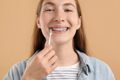 Photo of Girl with braces cleaning teeth with interdental brush on beige background