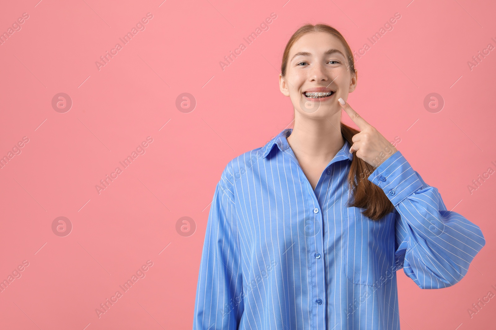 Photo of Girl pointing at her braces on pink background, space for text