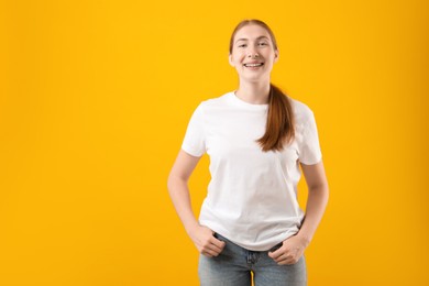 Photo of Smiling girl with braces on orange background, space for text