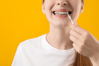 Photo of Girl with braces cleaning teeth with interdental brush on orange background, closeup