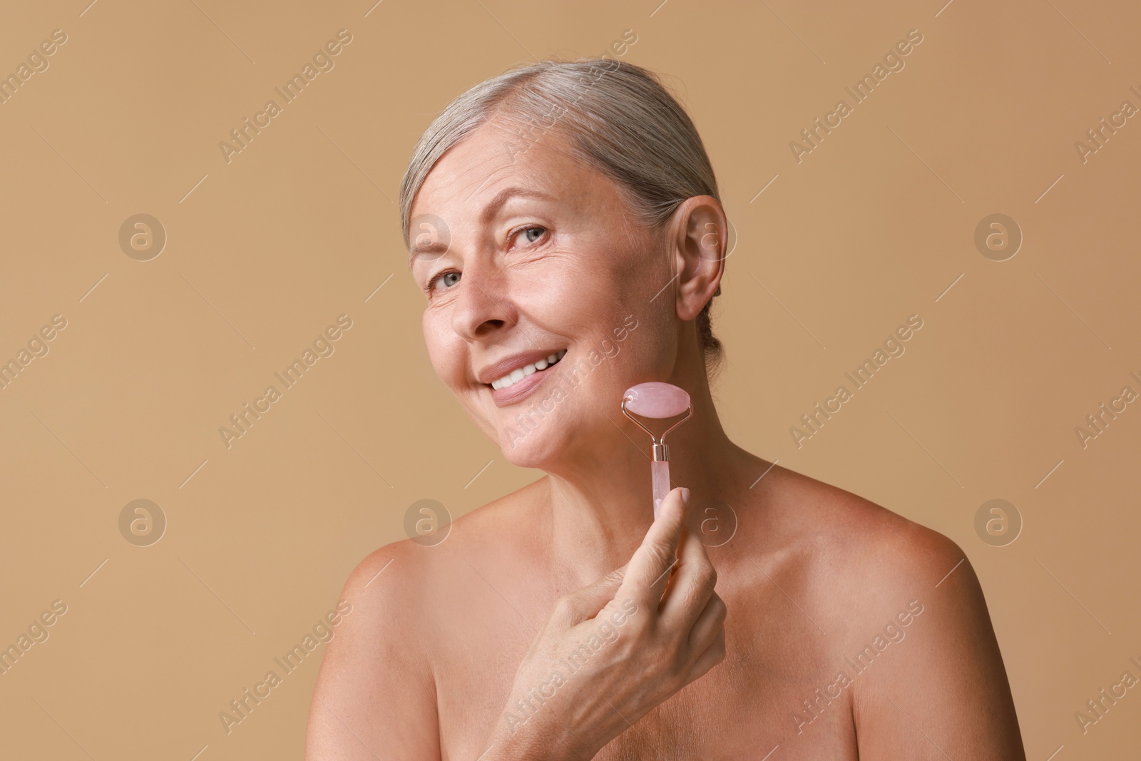 Photo of Beautiful woman doing facial massage with roller on beige background