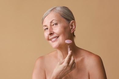 Beautiful woman doing facial massage with roller on beige background