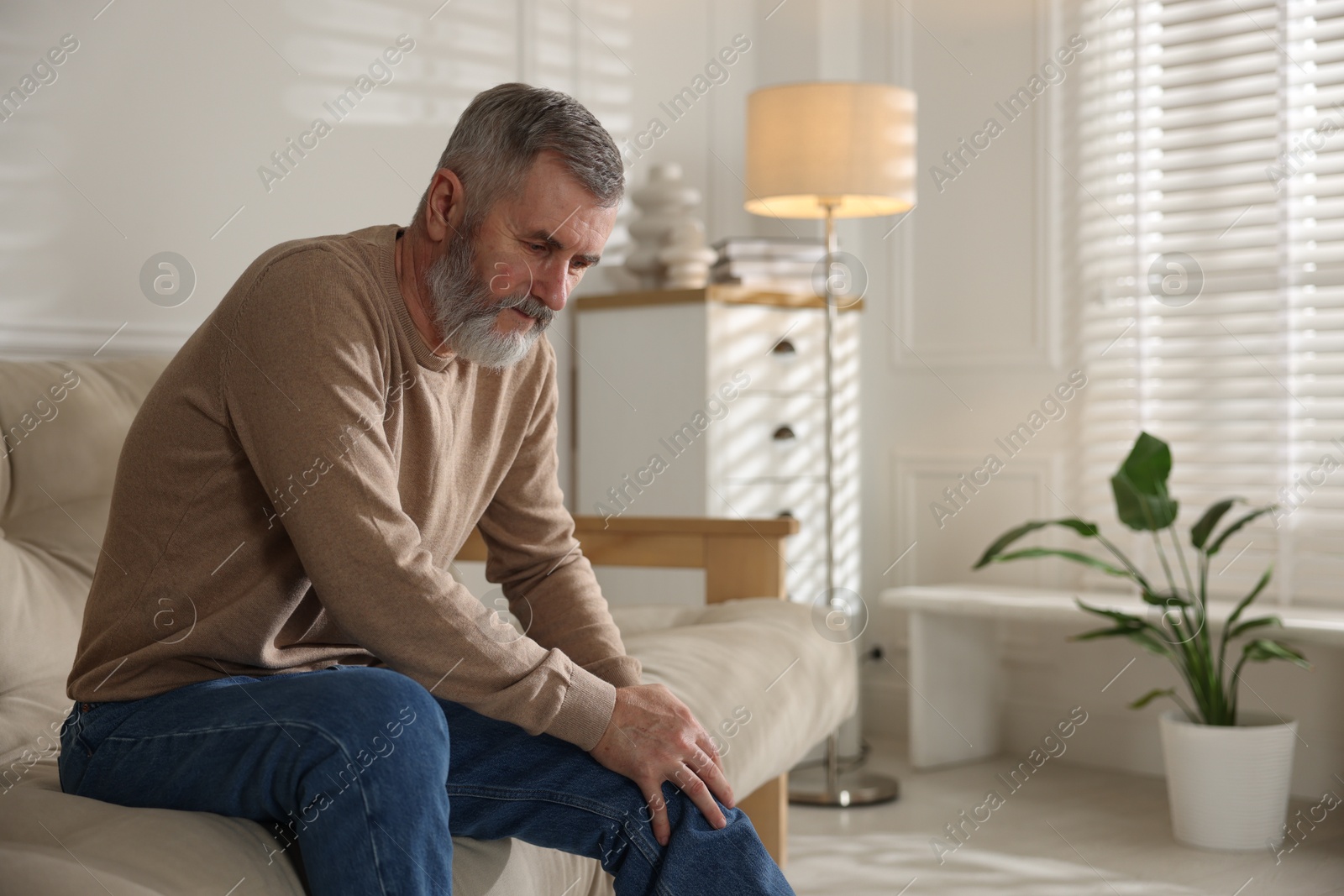 Photo of Senior man suffering from pain in knee on sofa at home