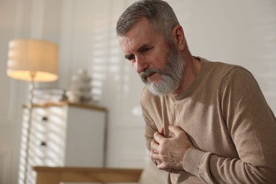 Senior man suffering from pain in chest at home, space for text