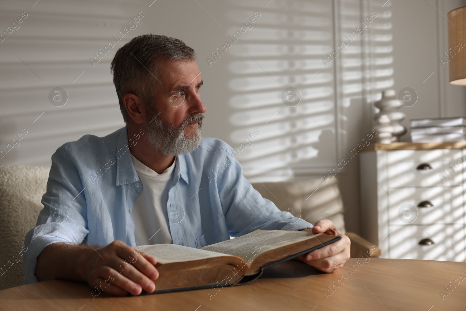 Photo of Senior man reading book at table indoors