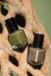 Nail polishes in bottles and piece of decorative wood on green background, top view