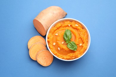 Photo of Tasty mashed sweet potato with basil, seeds in bowl and cut vegetable on blue background, flat lay