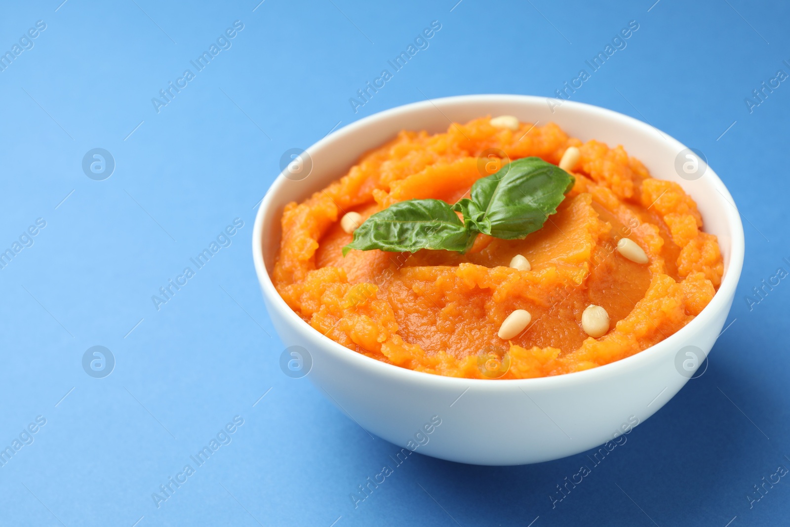 Photo of Tasty mashed sweet potato with basil and seeds in bowl on blue background, closeup