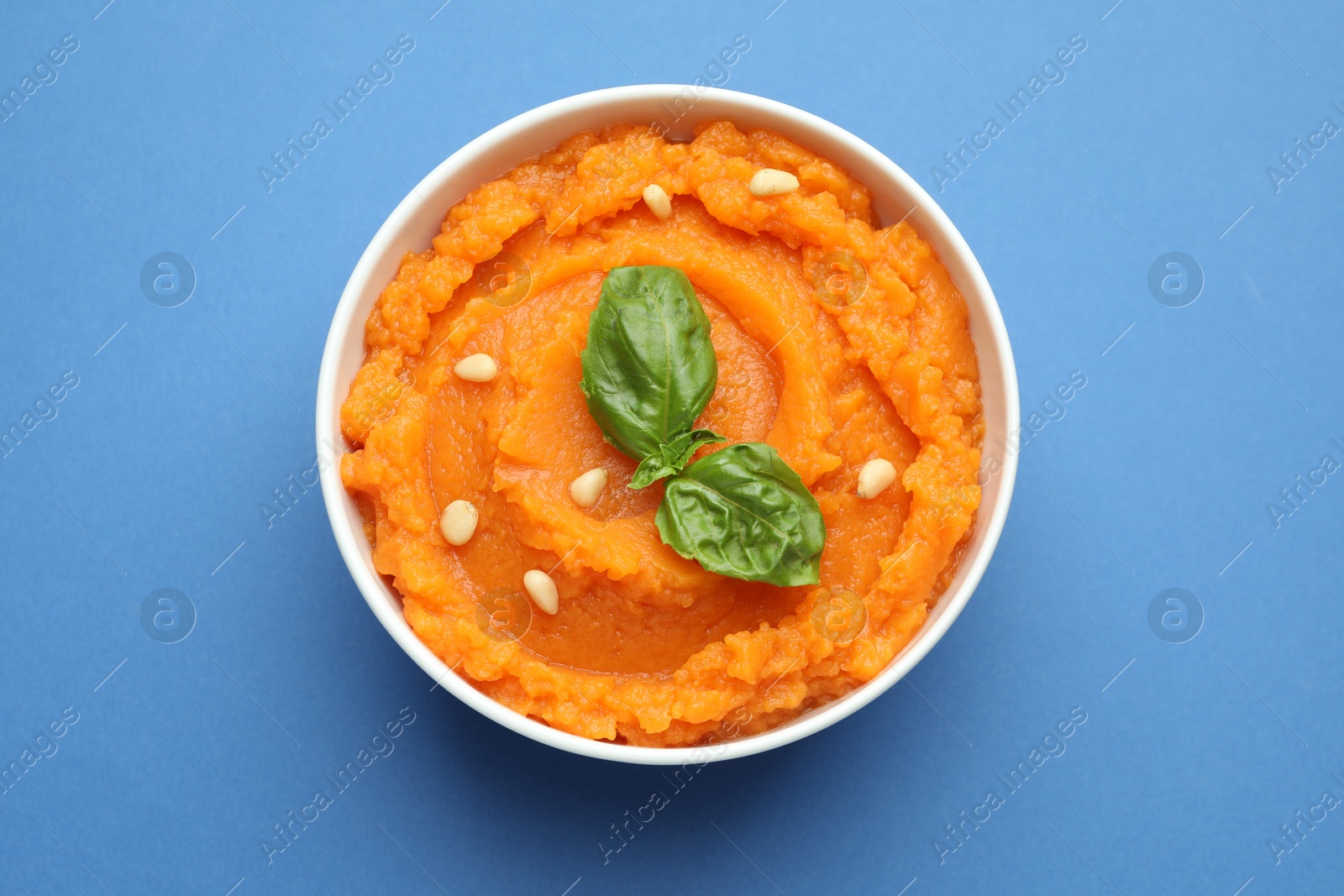 Photo of Tasty mashed sweet potato with basil and seeds in bowl on blue background, top view