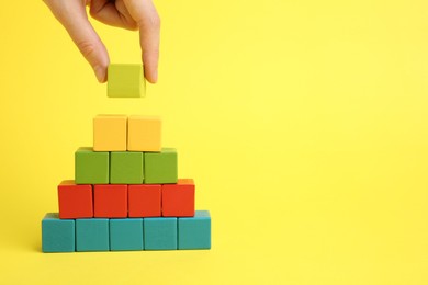 Photo of Woman building pyramid of cubes on yellow background, closeup. space for text