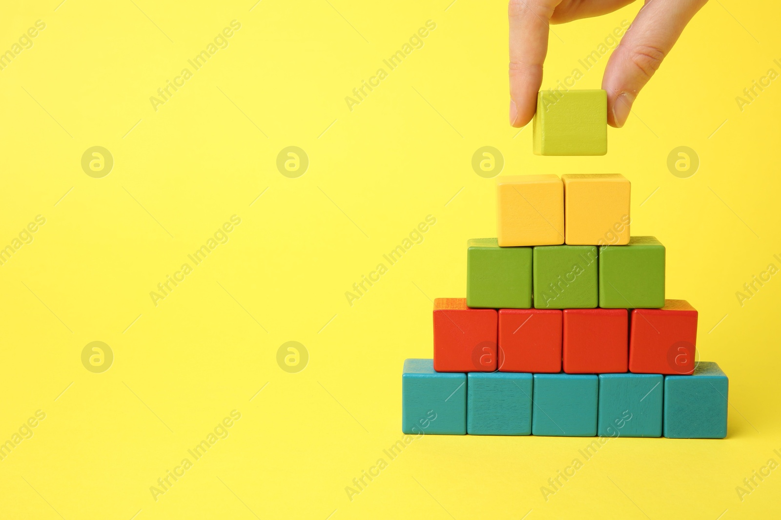 Photo of Woman building pyramid of cubes on yellow background, closeup. space for text