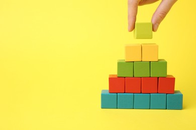 Photo of Woman building pyramid of cubes on yellow background, closeup. space for text