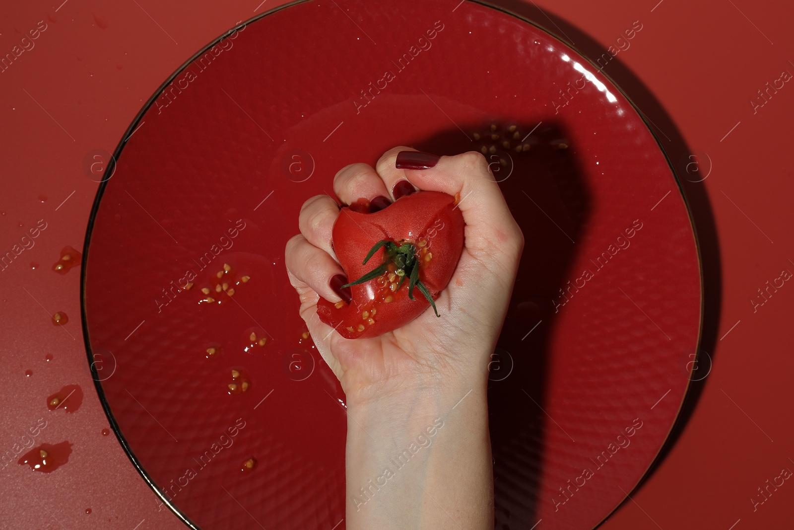 Photo of Woman smashing tomato on red background, top view