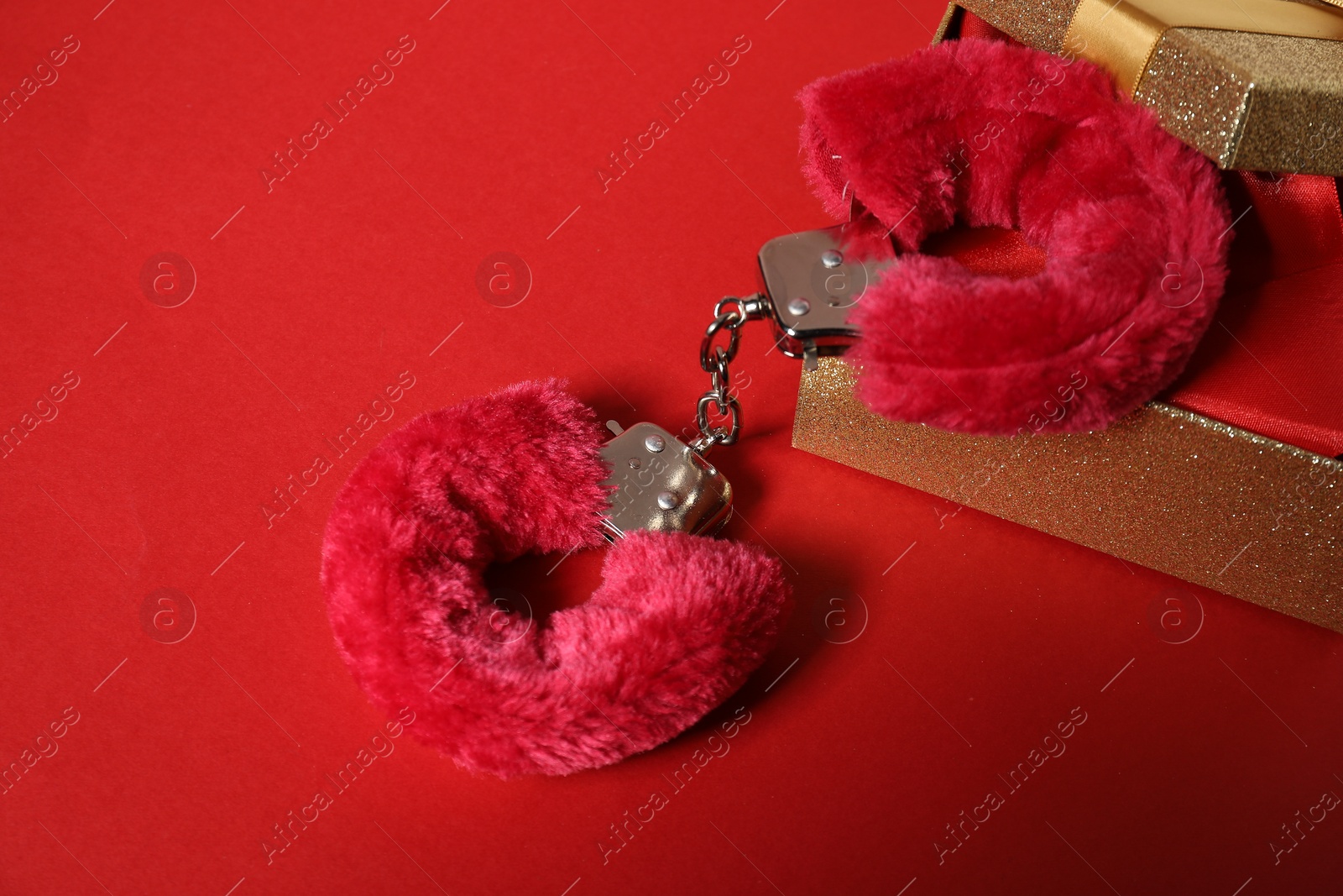 Photo of Bright fluffy handcuffs and gift box on red background, space for text