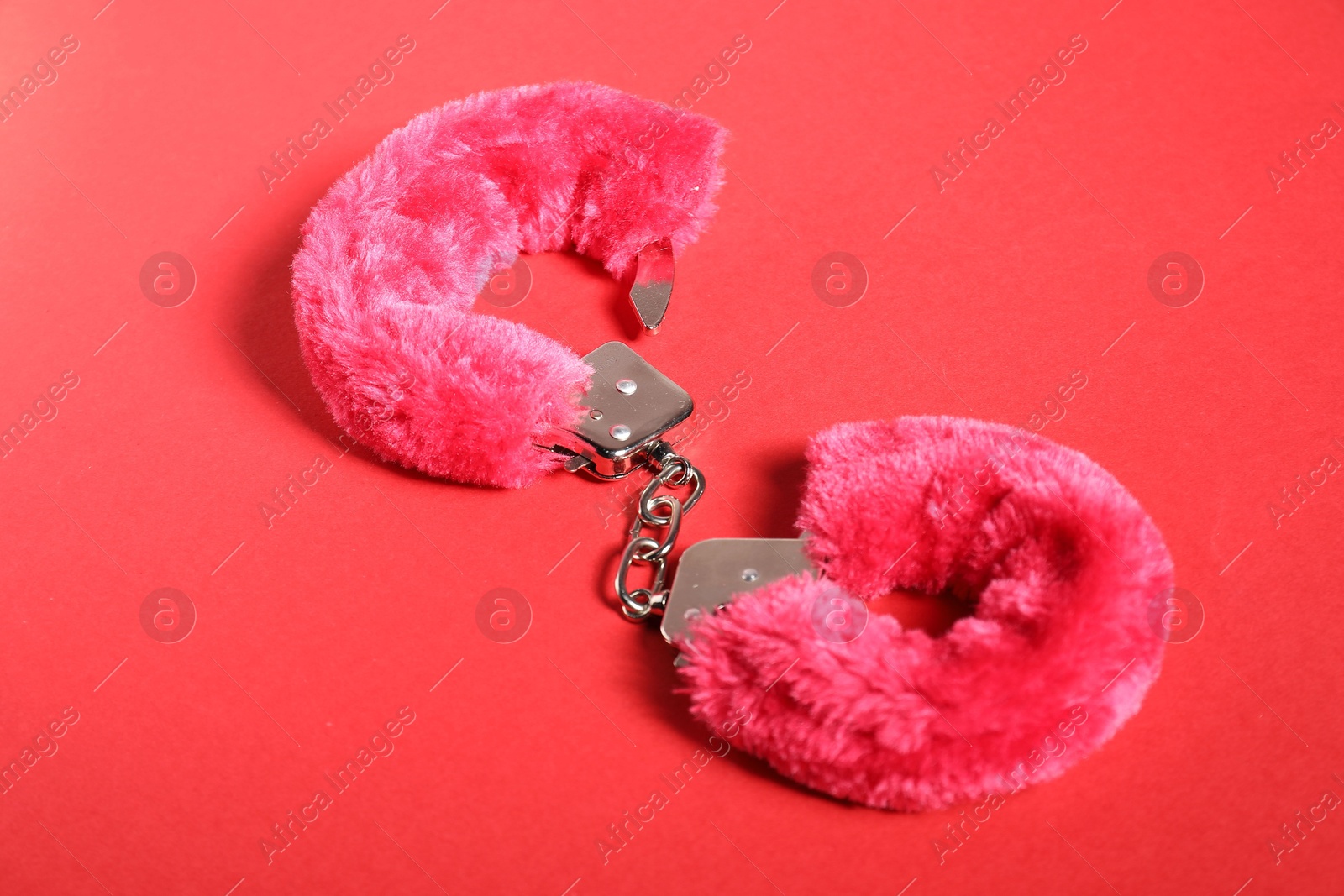 Photo of Pink fluffy handcuffs on red background. Sex toy