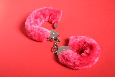 Photo of Pink fluffy handcuffs on red background. Sex toy