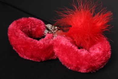 Photo of Bright fluffy handcuffs and red feather on black background, closeup