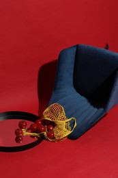 Creative still life with overturned dark blue armchair, net bag, tomatoes and mirror on red background