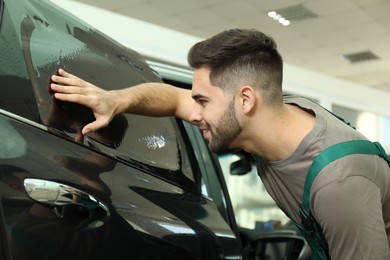 Worker tinting car window with foil in workshop