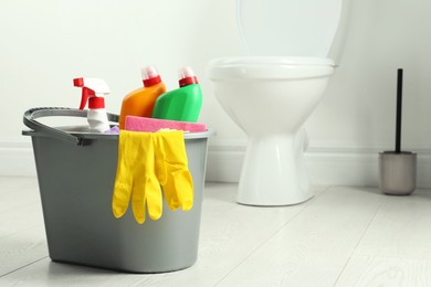 Photo of Bucket with different toilet cleaners and gloves on floor in bathroom