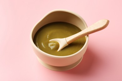 Photo of Delicious baby food with spoon in bowl on pink table