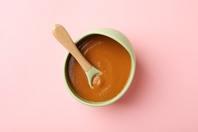 Photo of Delicious baby food with spoon in bowl on pink table, top view