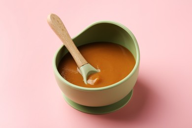 Photo of Delicious baby food with spoon in bowl on pink table