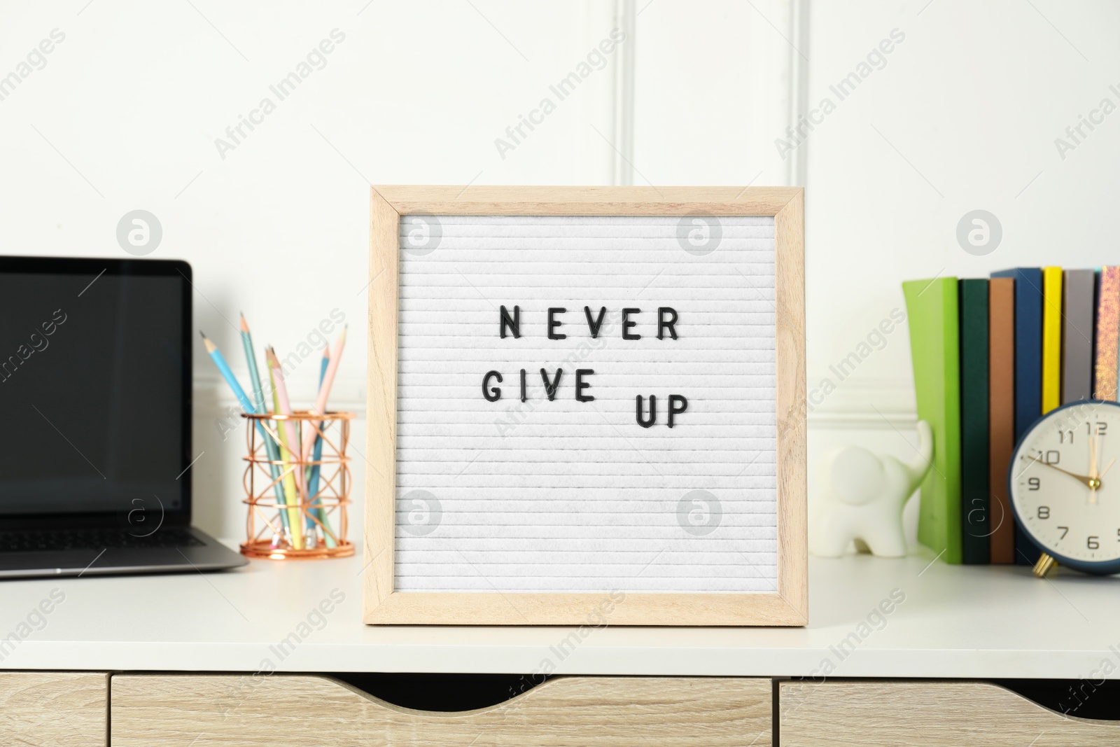 Photo of Letter board with phrase Never Give Up, laptop, alarm clock and stationery on white desk