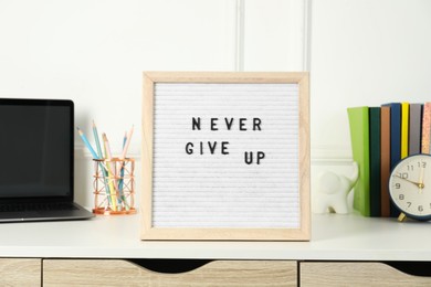 Photo of Letter board with phrase Never Give Up, laptop, alarm clock and stationery on white desk