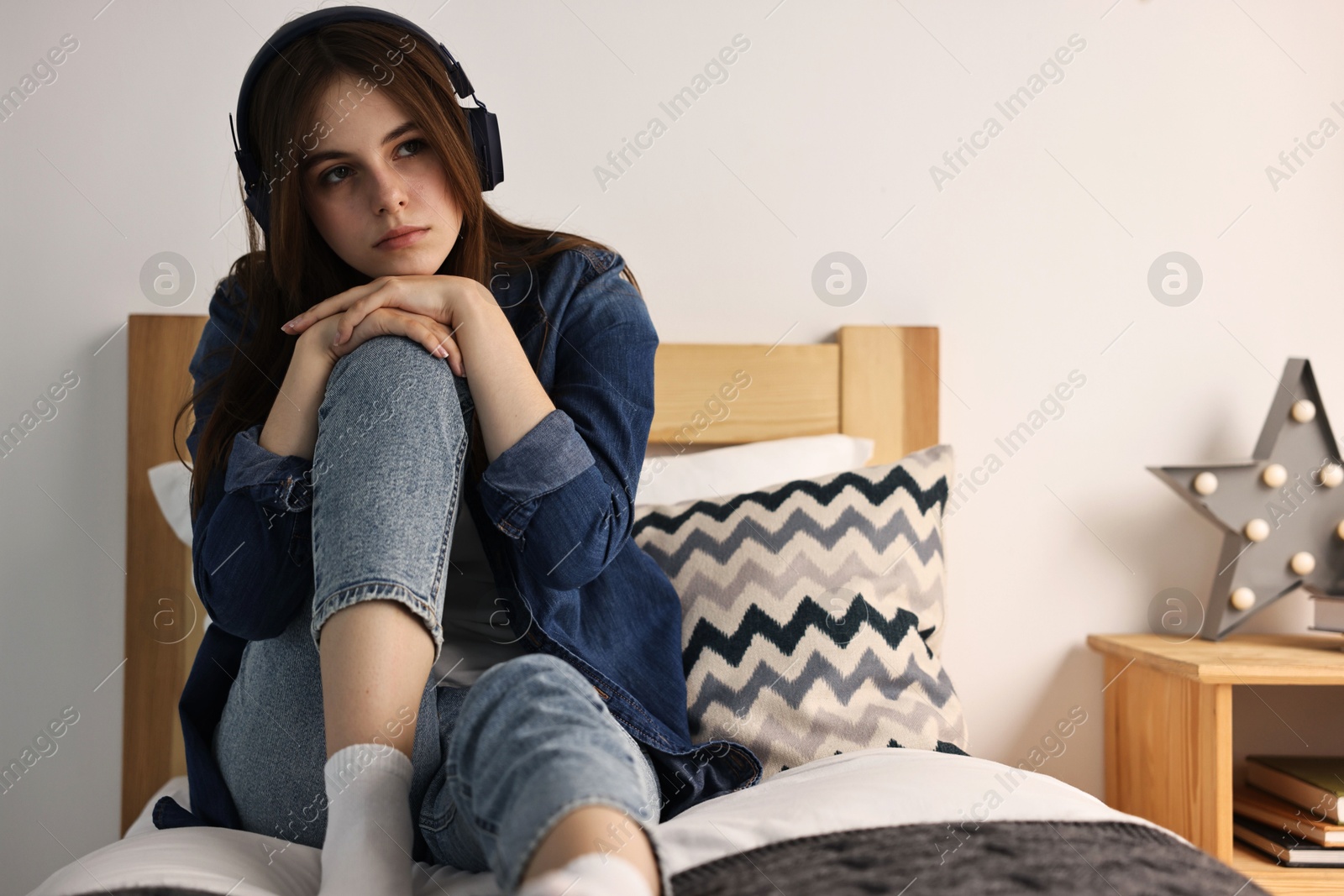 Photo of Loneliness concept. Sad teenage girl in headphones listening to music on bed at home