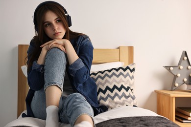 Photo of Loneliness concept. Sad teenage girl in headphones listening to music on bed at home