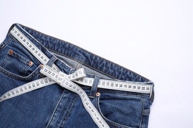 Photo of Jeans and measuring tape on white background, top view