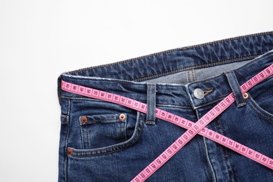 Photo of Jeans and measuring tape on white background, top view