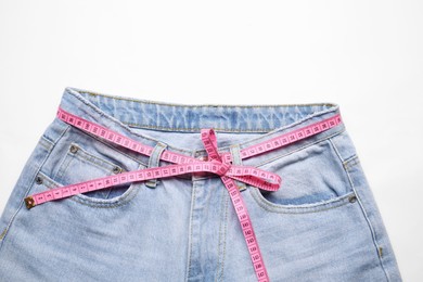 Photo of Jeans and measuring tape on white background, top view