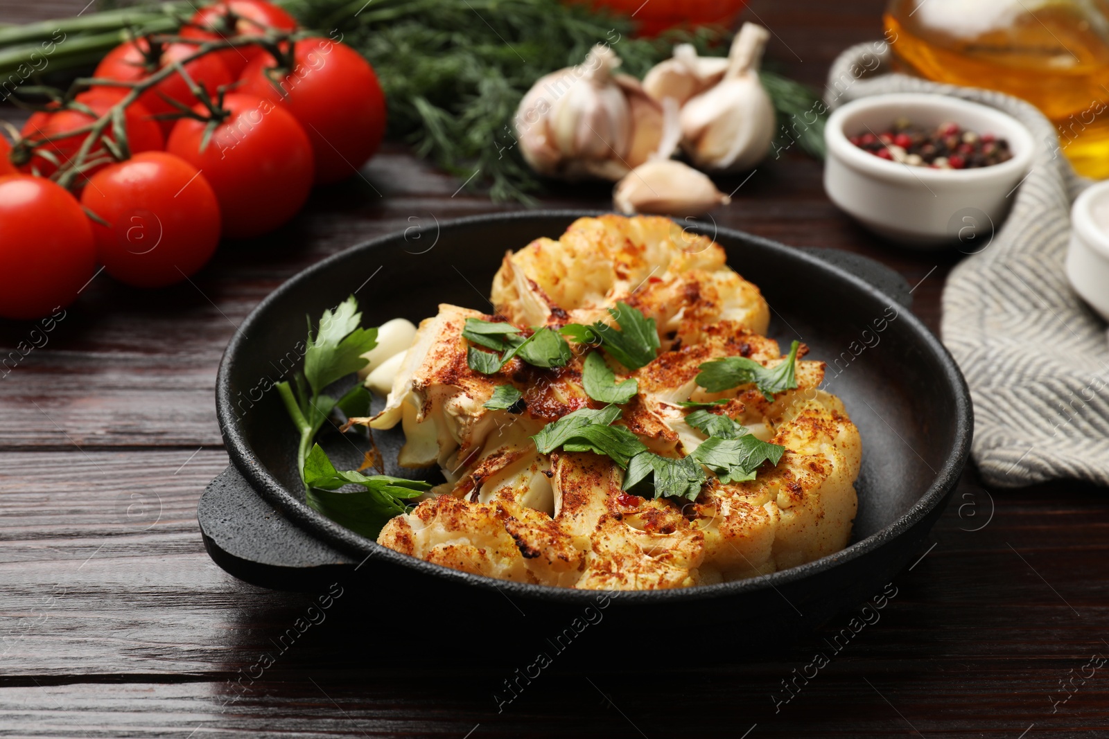 Photo of Tasty cauliflower steak in frying pan and other products on wooden table, closeup