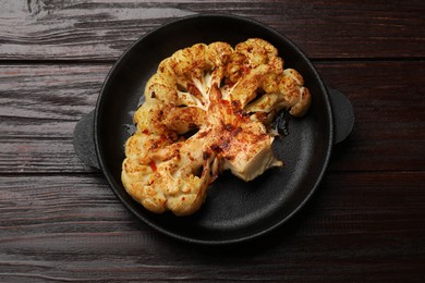 Photo of Tasty cauliflower steak in frying pan on wooden table, top view